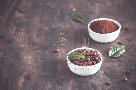 coffee beans and ground coffee in bowls with coffee tree leaf on a dark background..copy space for your textの写真素材