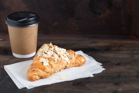 fresh croissant and coffee in a paper cup on a dark background.の写真素材