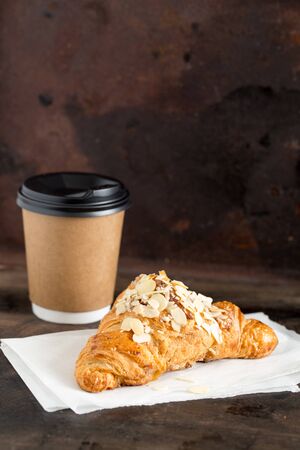 fresh croissant and coffee in a paper cup on a dark background.の写真素材