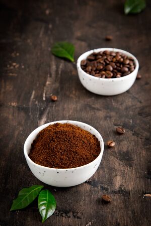 coffee beans and ground coffee in bowls with coffee tree leaf on a dark background..の写真素材