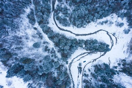Winter forest with frosty trees and a little meandering stream, aerial viewの写真素材