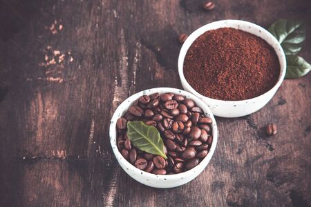 coffee beans and ground coffee in bowls with coffee tree leaf on a dark background..の写真素材