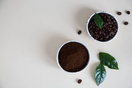 coffee beans and ground coffee in bowls with coffee tree leaf on a light background..copy space for your textの写真素材