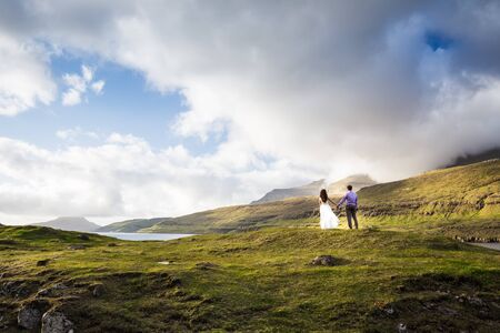 A happy couple in wedding dresses or the bride and groom holding hands and looking at the picturesque nature. Faroe Islands/の写真素材