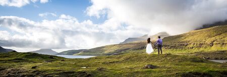 A happy couple in wedding dresses or the bride and groom holding hands and looking at the picturesque nature. Faroe Islands/の写真素材