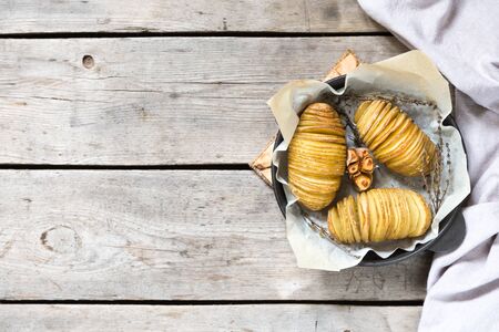 Hasselback potatoes. Baked potatoes in pan on wooden table/