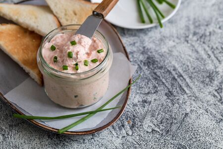 Salmon and soft creme cheese spread in jar. Salmon rillettes, mousse, pate and toasts on gray...