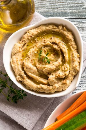 hummus sauce in a bowl, sesame seeds, olive oil, cucumber and carrots on a light backgroundの写真素材