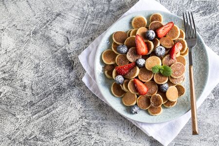Tiny pancakes for breakfast. Cereal pancakes with blueberries, strawberries in plate on grey background. Trendy food. Copy space for text or designの写真素材