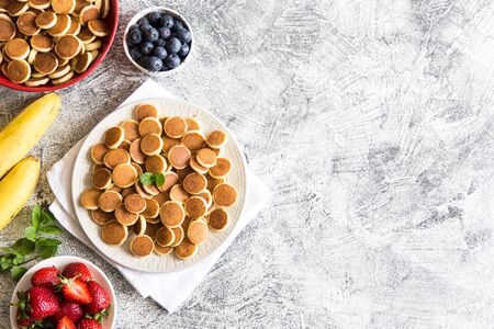 Tiny pancakes for breakfast. Cereal pancakes with blueberries, bananas, strawberries on grey background. Trendy food. Copy space for text or designの写真素材