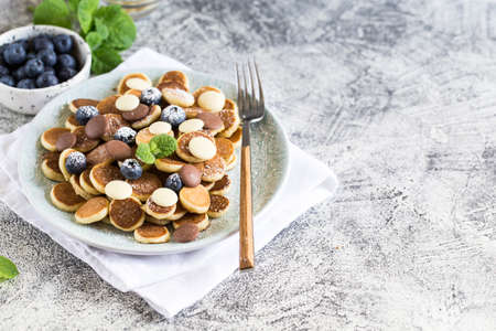 Tiny pancakes for breakfast. Cereal pancakes with blueberries and chocolate drops in plate on gray background. Trendy food. Copy space for text or designの写真素材