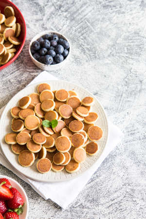 Tiny pancakes for breakfast. Cereal pancakes with blueberries, bananas, strawberries on gray background. Trendy food. Copy space for text or designの写真素材