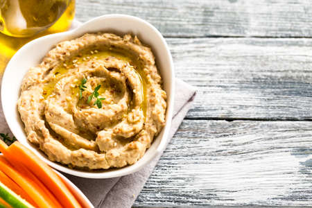 hummus sauce in a bowl, sesame seeds, olive oil, cucumber and carrots on a light backgroundの写真素材