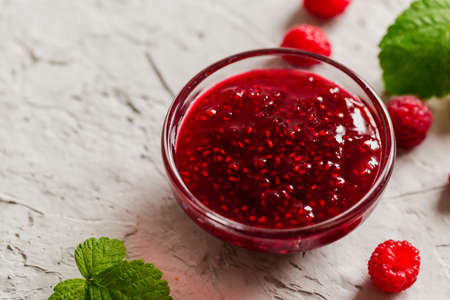 homemade raspberry jam on a concrete background with fresh raspberries, selective focus.