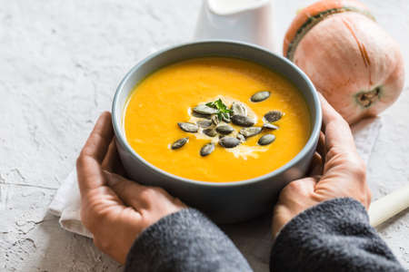 pumpkin and carrot cream soup with pumpkin seeds and toasted bread. female hands holding a plateの写真素材