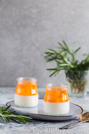 homemade panna cotta with slices of peach and peach jelly in glass jars on a gray concrete background.の写真素材