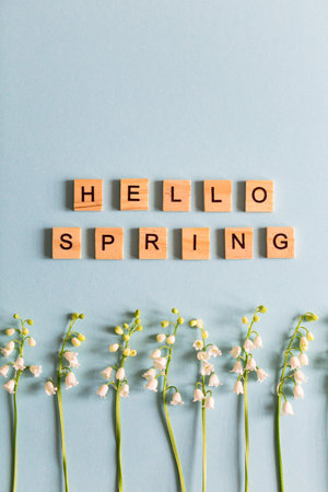 lilies of the valley on a blue photo and text in wooden letters hello spring.