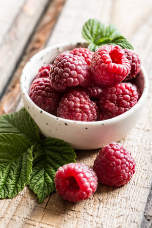 fresh juicy raspberries with green leaves in a plate on a wooden table.の写真素材