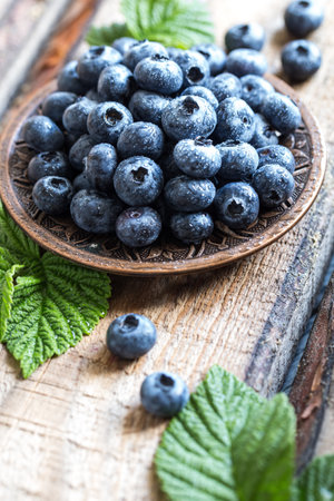 fresh juicy blueberries with green leaves in a plate on a wooden table.の写真素材