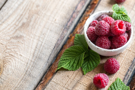 fresh juicy raspberries with green leaves in a plate on a wooden table.の写真素材