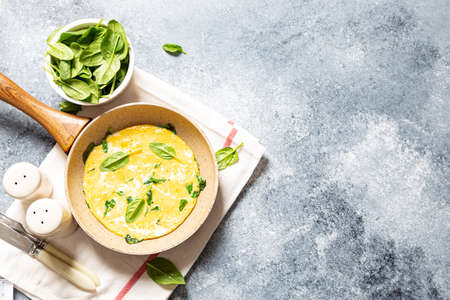 homemade egg omelet with spinach in a frying pan on a gray concrete backgroundの写真素材