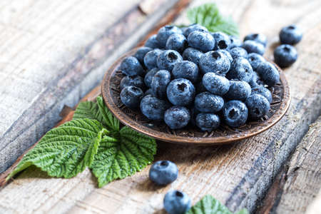 fresh juicy blueberries with green leaves in a plate on a wooden table.の写真素材