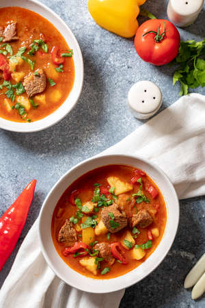 goulash is a traditional Hungarian dish with beef, potatoes, tomatoes and peppers. goulash in white plates with vegetables for cooking.の写真素材
