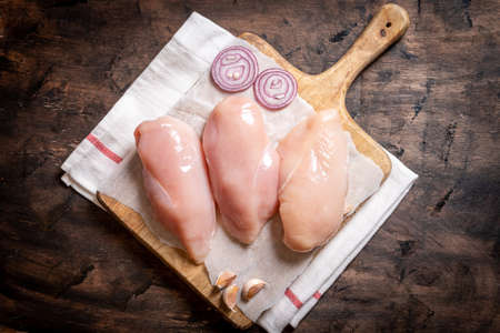 raw chicken breasts on a cutting board and wood background with onion and garlic.の写真素材