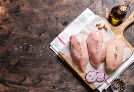 raw chicken breasts on a cutting board and wood background with onion and garlic.の写真素材