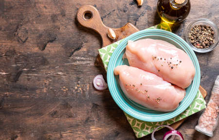 raw chicken breasts on a plate and wood background with onion and garlic.の写真素材