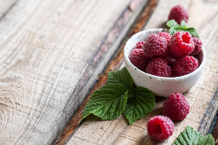 fresh juicy raspberries with green leaves in a plate on a wooden table.の写真素材