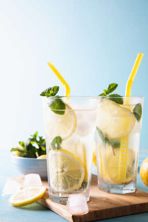 Two glass with lemonade or mojito cocktail with lemon and mint, cold refreshing drink or beverage with ice on blue background. Copy space.の写真素材
