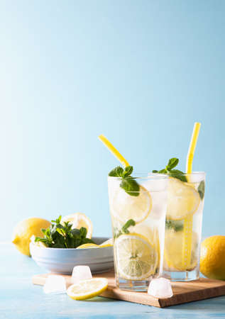 Two glass with lemonade or mojito cocktail with lemon and mint, cold refreshing drink or beverage with ice on blue background. Copy space.の写真素材