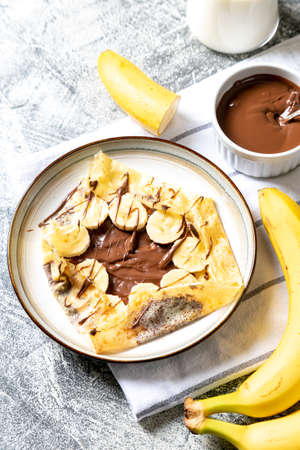 Crepes, thin pancakes on a plate. Chocolate hazelnut spread and banana filled crepes on plate. Tasty crepes or blini with sweet sauce.の写真素材
