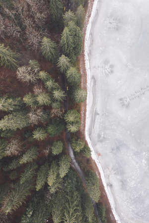 aerial view from a drone of a forest in the snow, and a frozen icy lake.の写真素材