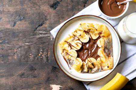 Crepes, thin pancakes on a plate. Chocolate hazelnut spread and banana filled crepes on plate. Tasty crepes or blini with sweet sauce.の写真素材