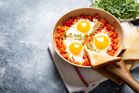 Tasty and Healthy Shakshuka in a Frying Pan. Eggs Poached in Spicy Tomato Pepper Sauce. fried eggs with toast, arugulaの写真素材
