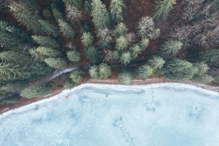 aerial view from a drone of a forest in the snow, and a frozen icy lake.の写真素材
