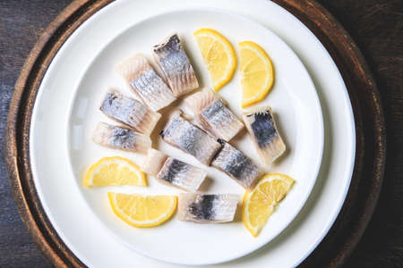 Salted herring with lemon on plate on wooden background with copy space. Marinated sliced fish. Food with healthy unsaturated fats, Omega 3. Top view, flat layの写真素材