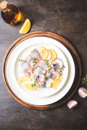 Salted herring with spice, herbs and onion on plate on wooden background with copy space. Marinated sliced fish. Food with healthy unsaturated fats, Omega 3. Top view, flat layの写真素材