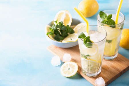 Two glass with lemonade or mojito cocktail with lemon and mint, cold refreshing drink or beverage with ice on blue background. Copy space.の写真素材