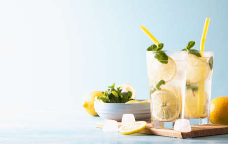 Two glass with lemonade or mojito cocktail with lemon and mint, cold refreshing drink or beverage with ice on blue background. Copy space.の写真素材