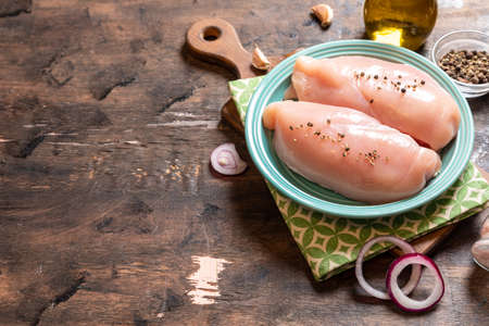 raw chicken breasts on a plate and wood background with onion and garlic.の写真素材