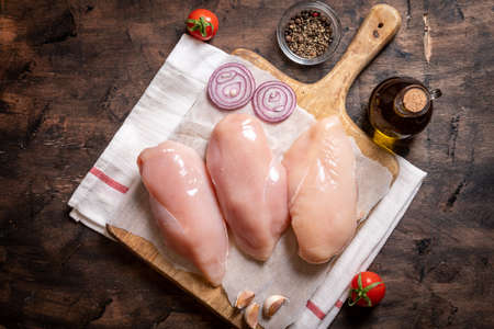 raw chicken breasts on a cutting board and wood background with onion and garlic.の写真素材