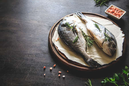 fresh raw dorado fish on a cutting wood board with pink himalayan salt, pink peppercorns and rosemaryの写真素材