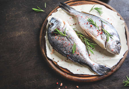 fresh raw dorado fish on a cutting wood board with pink himalayan salt, pink peppercorns and rosemaryの写真素材