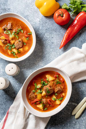 goulash is a traditional Hungarian dish with beef, potatoes, tomatoes and peppers. goulash in white plates with vegetables for cooking.の写真素材