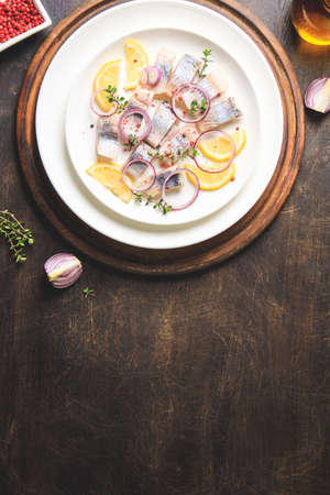 Salted herring with spice, herbs and onion on plate on wooden background with copy space. Marinated sliced fish. Food with healthy unsaturated fats, Omega 3. Top view, flat layの写真素材