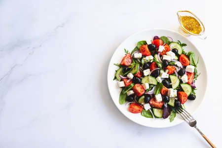 Greek salad of fresh cucumber, tomato, red onion, feta cheese and olives with olive oil. Salad with vegetables and greens. Healthy food, top viewの写真素材