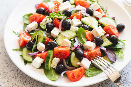 Greek salad of fresh cucumber, tomato, red onion, feta cheese and olives with olive oil. Salad with vegetables and greens. Healthy food, top viewの写真素材